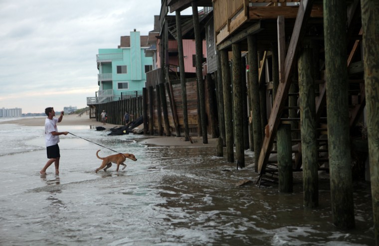 Chic's Beach resident Taylor Sharpe and his dog Sandy walk the beach there at high tide on Aug. 28, 2011, after the departure of Hurricane Irene. Waves from the Chesapeake Bay lap at the pilings of the waterfront homes on Ocean View Avenue in this section of Virginia Beach. (Vicki Cronis-Nohe | The Virginian-Pilot)